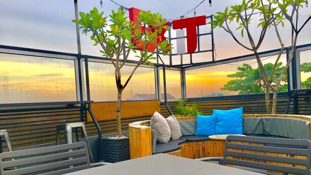 Un espace extérieur accueillant avec une table et des chaises, une tasse de café et une vue sur le coucher du soleil à travers de grandes fenêtres.