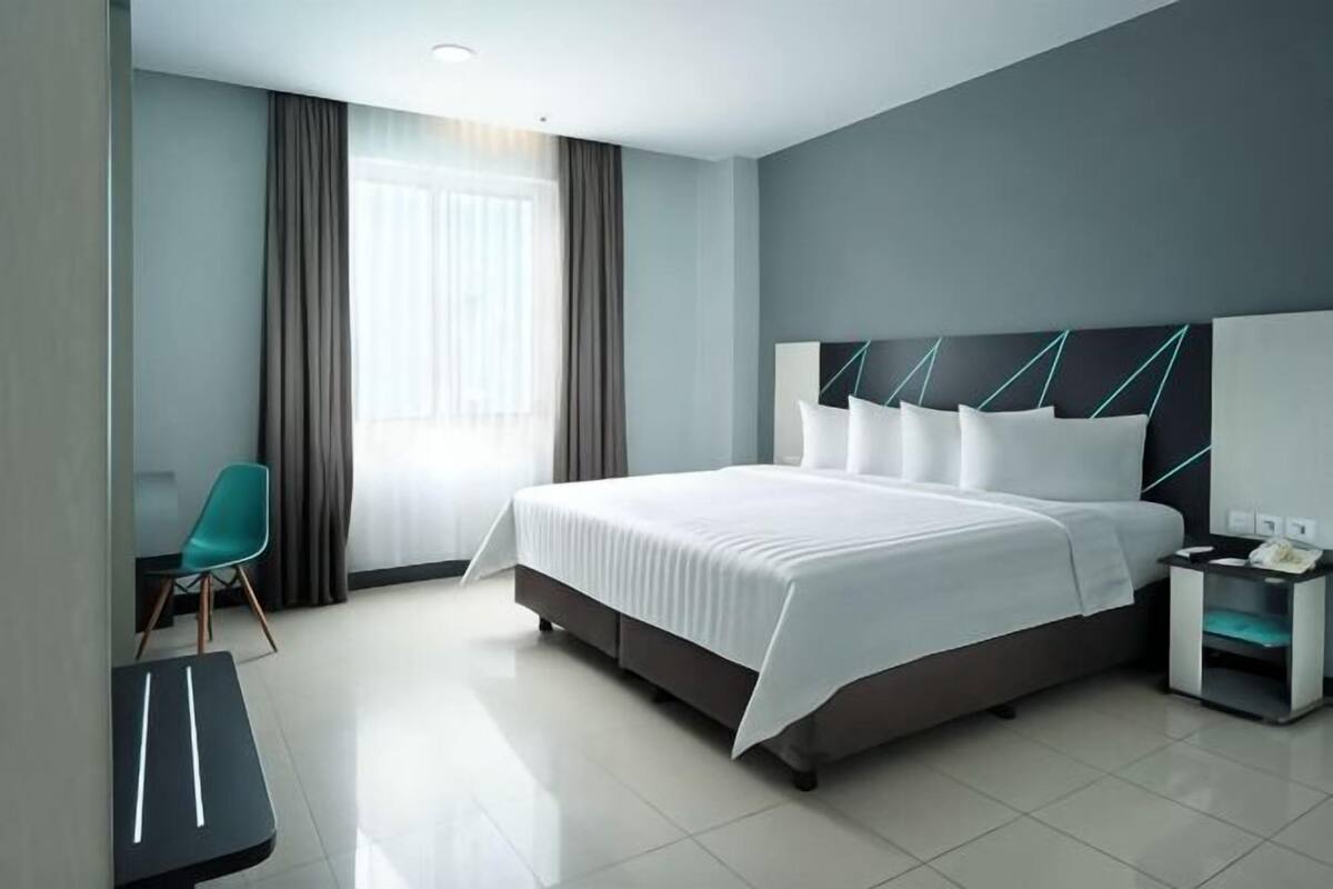 A modern hotel room with a large bed, a desk, a chair, and a nightstand.