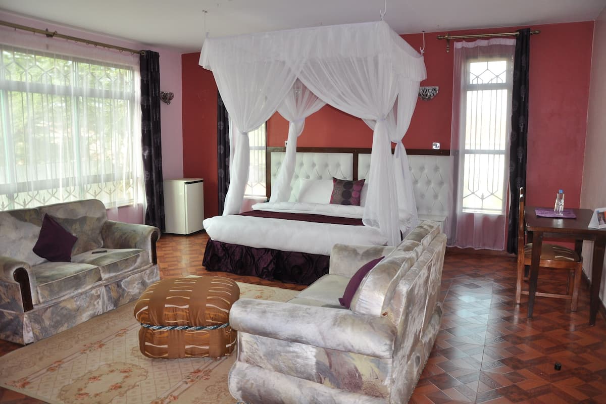 A bedroom with a four-poster bed, a sofa, a coffee table, and a bedside table with a lamp.