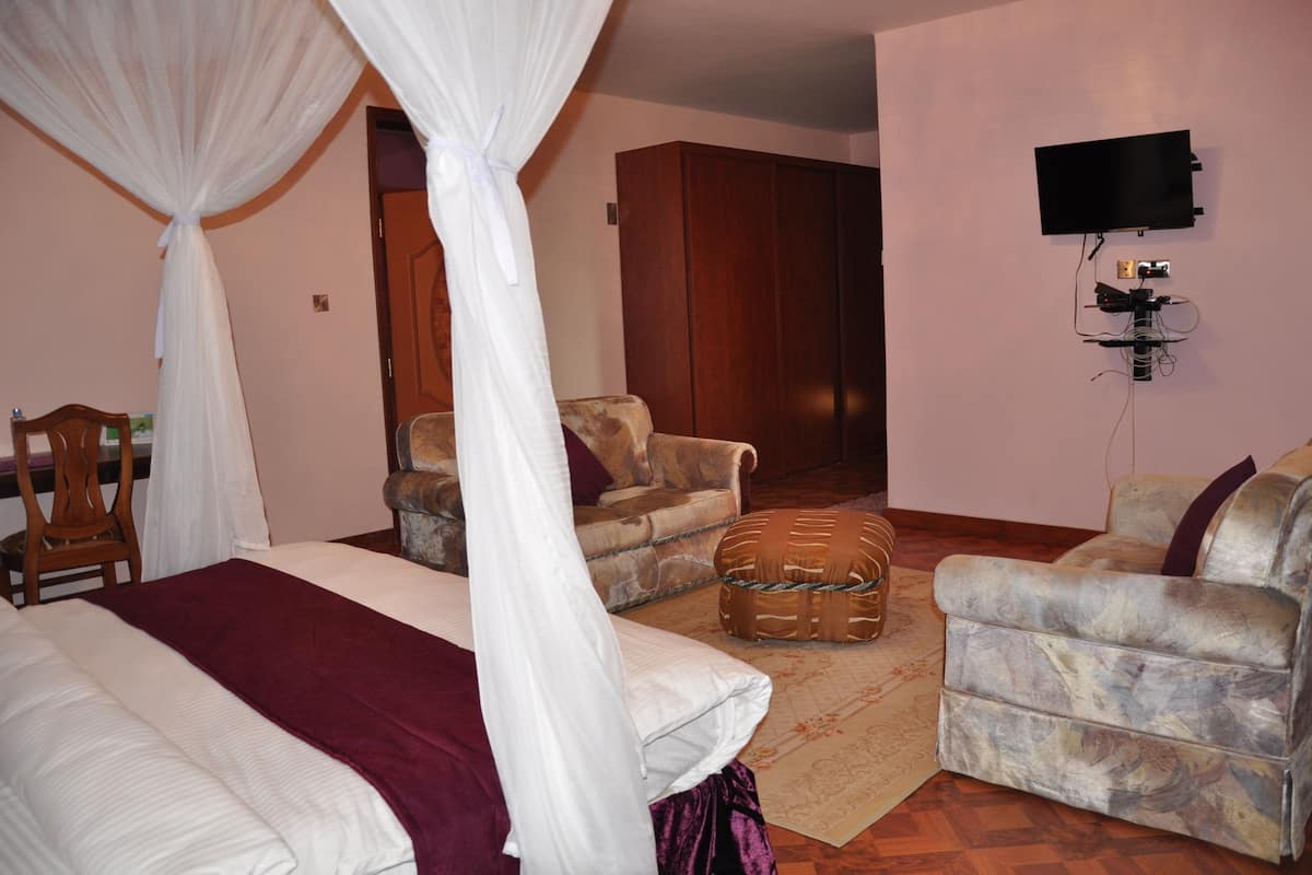 A bedroom with a four-poster bed, a sofa, a chair, and a television mounted on the wall.