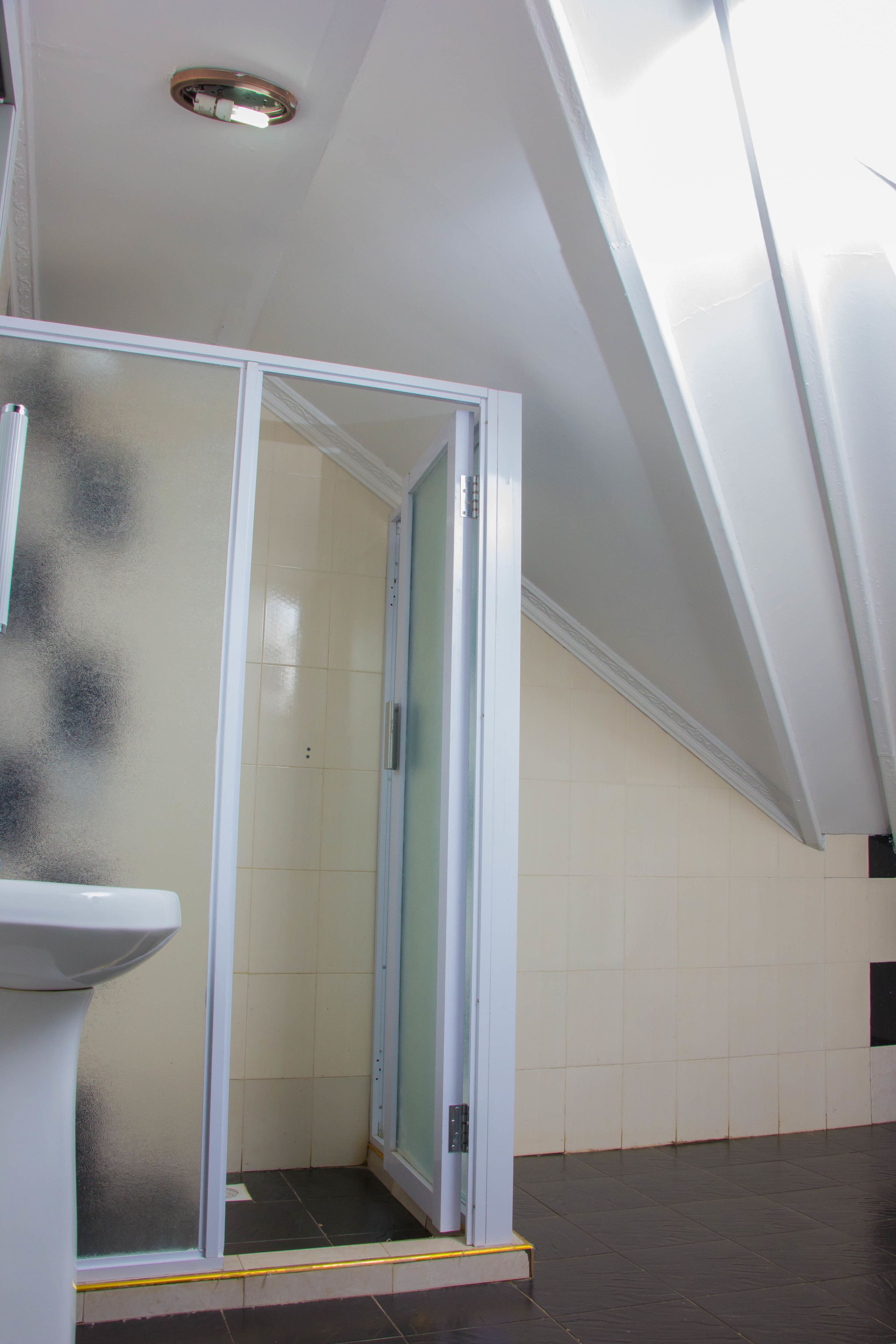 Eine Dusche mit gefrosteten Glastüren, ein weißes Waschbecken und ein gefliester Boden.