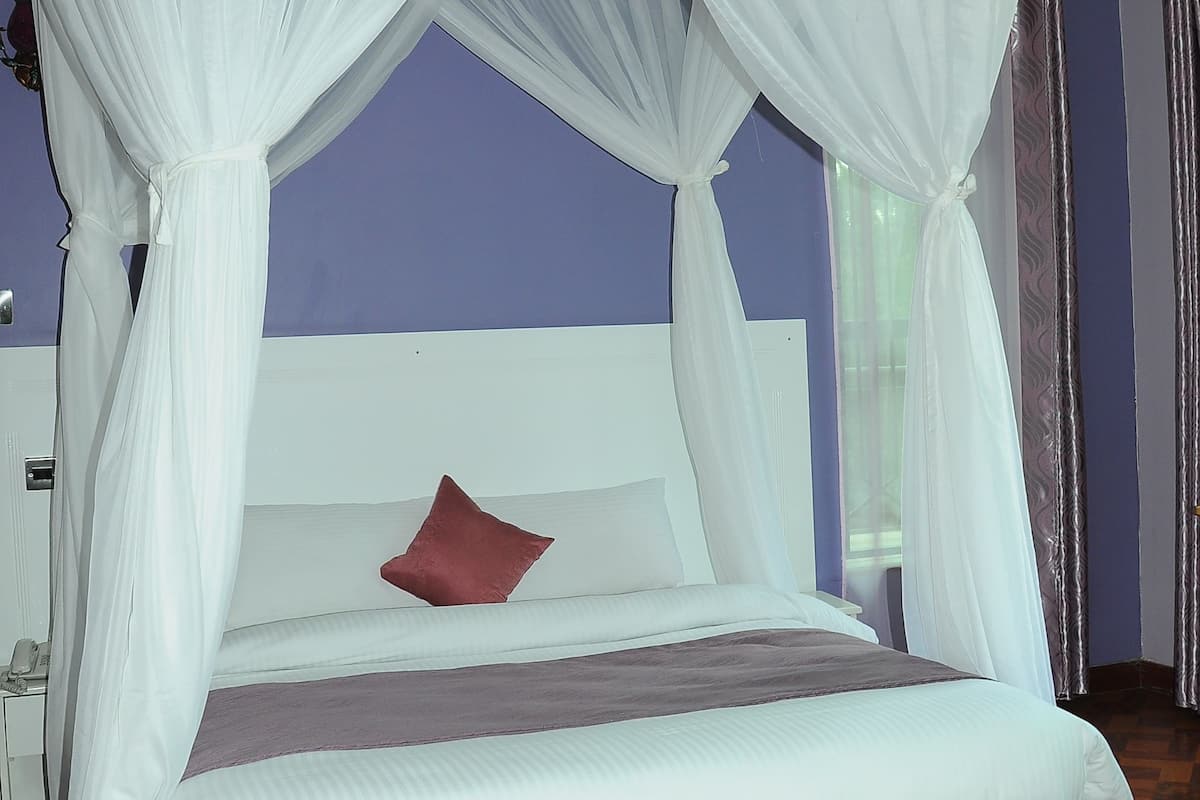 A bed with a canopy, a bedside table, and a window with curtains.