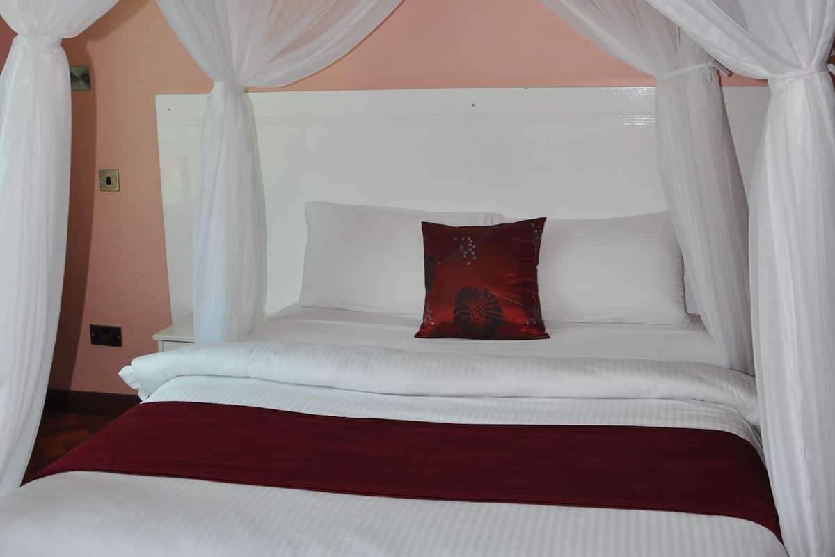 A bed with a canopy, white bedding, a red throw, and a wooden floor.