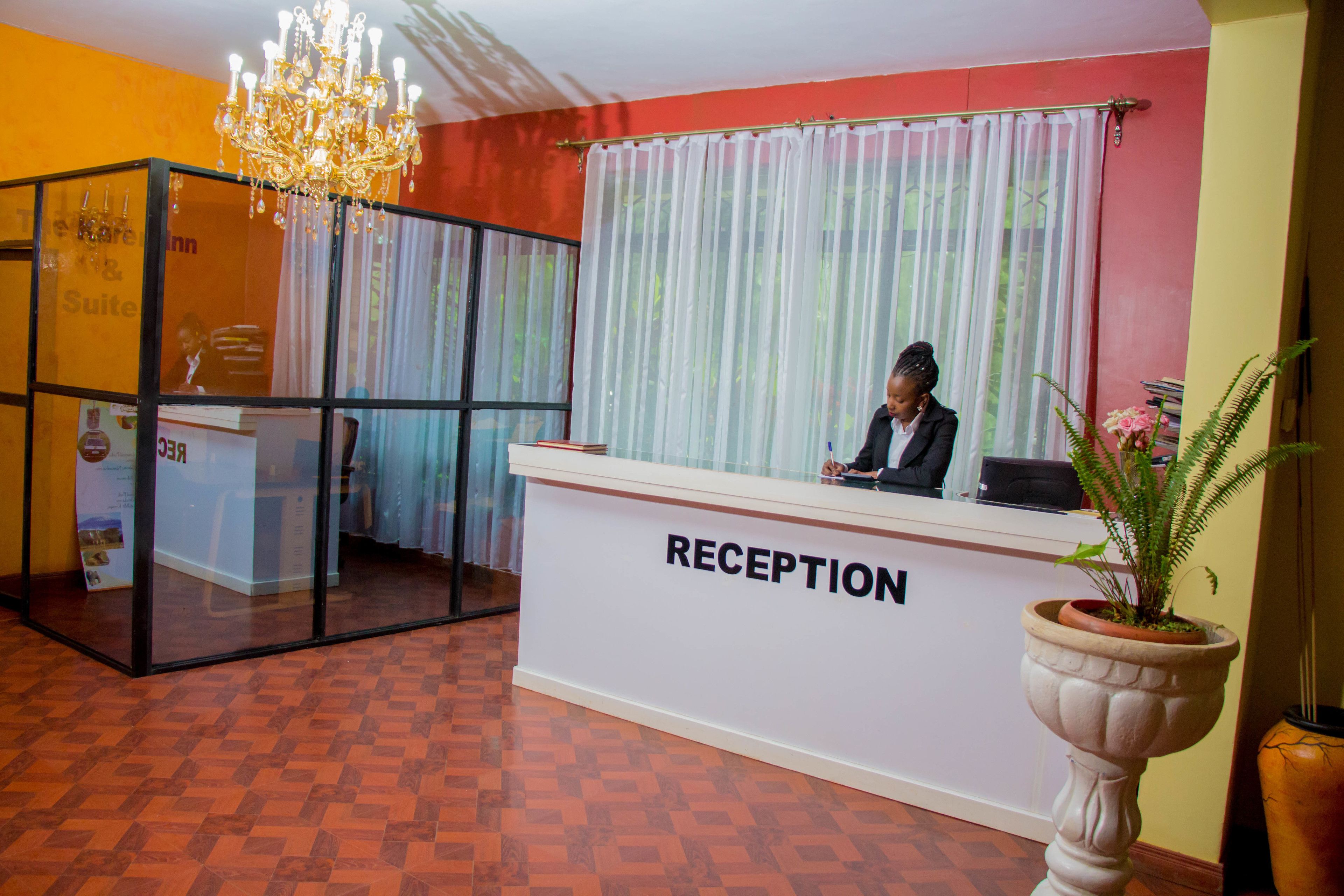 A reception area with a reception desk labeled "RECEPTION," a chandelier, a potted plant, and a glass partition with a sign that reads "Suite."