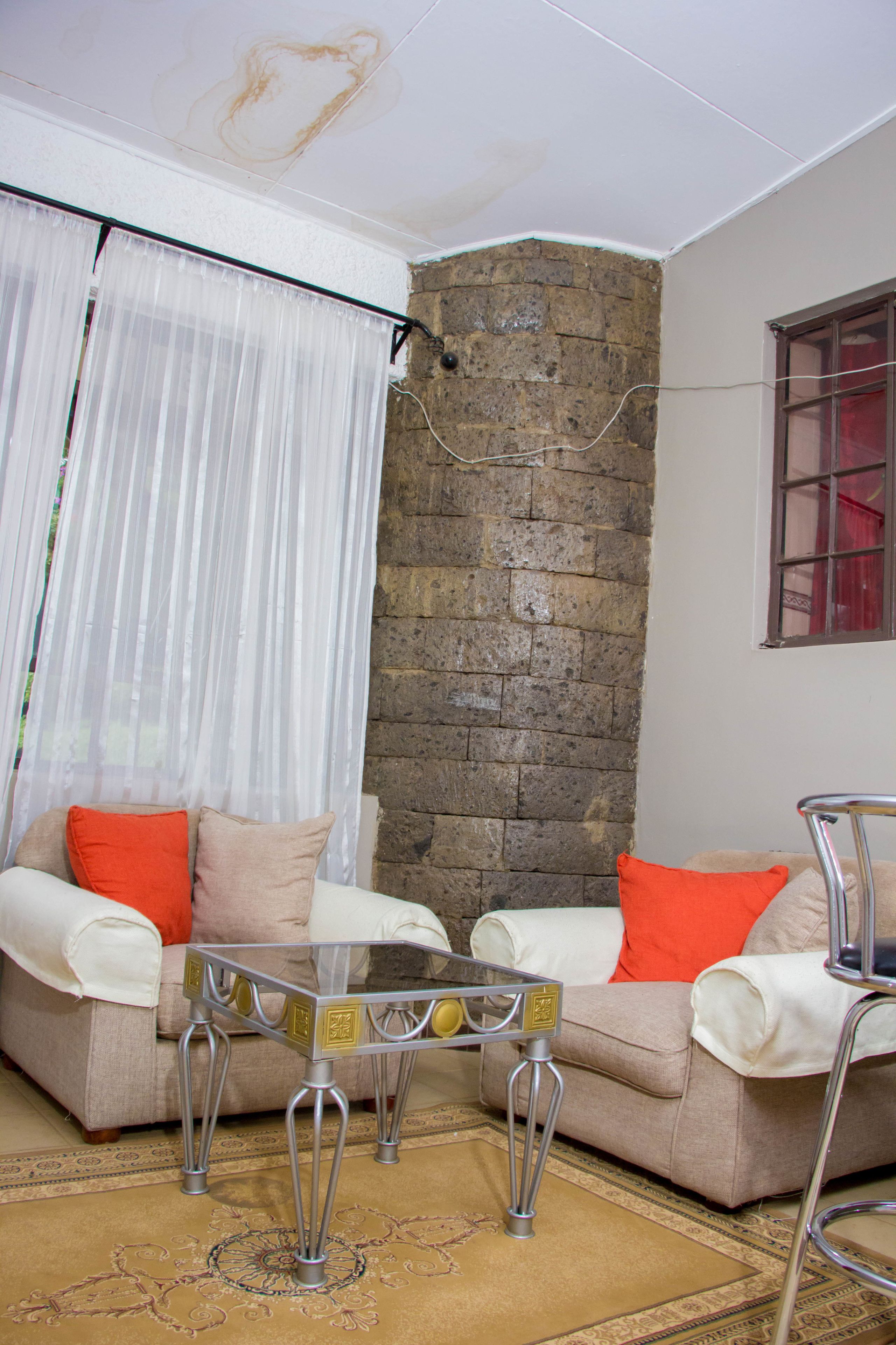 A living room with a stone wall, a glass coffee table, and a beige sofa with orange cushions.