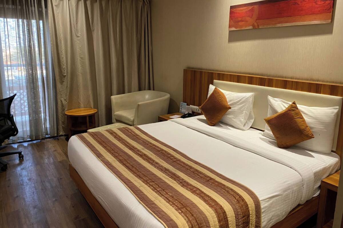 Habitación de hotel con una cama grande, una silla, una mesita de noche y un cuadro en la pared.