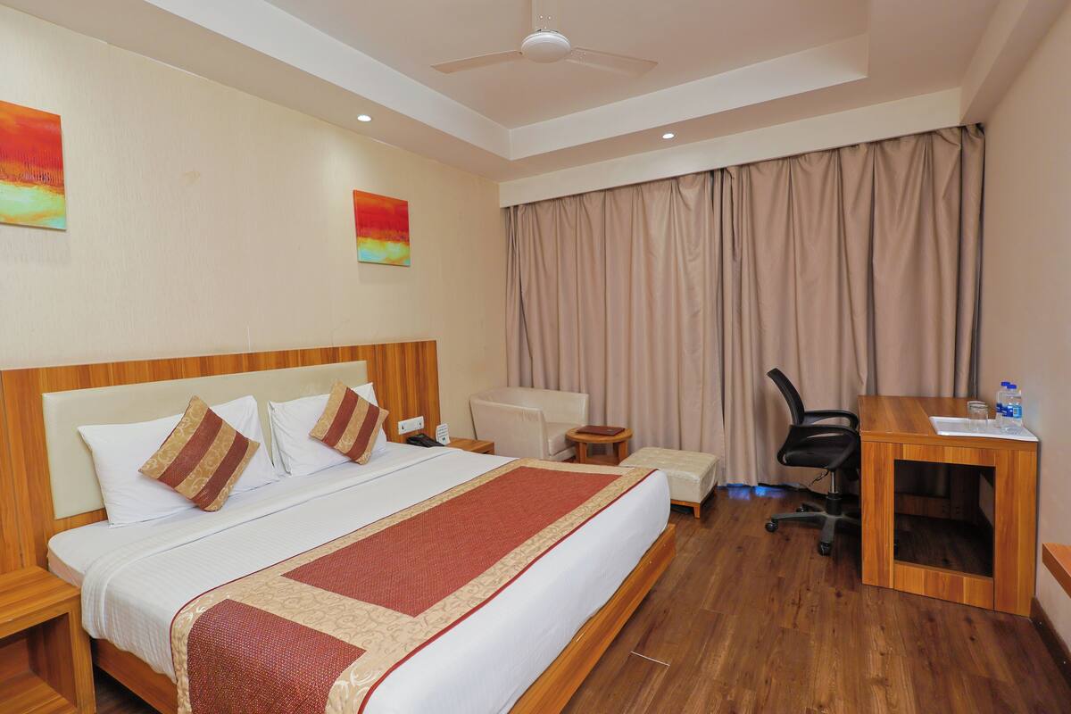 Una habitación de hotel con una cama grande, un escritorio, una silla y un ventilador de techo.