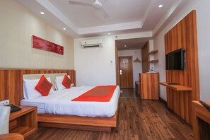 A hotel room with a bed, wooden furniture, a TV, and an air conditioning unit. - Le ROI Udaipur (Udaipur)