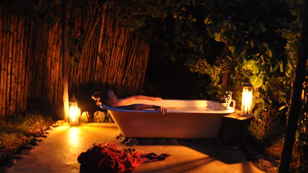 A person relaxing in a bathtub outdoors at night, surrounded by trees and lit by lanterns. - Mbweha Camp Lake Nakuru (Nakuru)