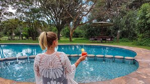 A woman sitting by a pool with a drink, surrounded by stone tiles and greenery. - Mbweha Camp Lake Nakuru (Nakuru)