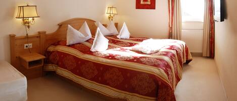 Une chambre avec un plafond en bois, deux tables de chevet avec des lampes, un lit avec une literie rouge et dorée, et une fenêtre avec des rideaux.