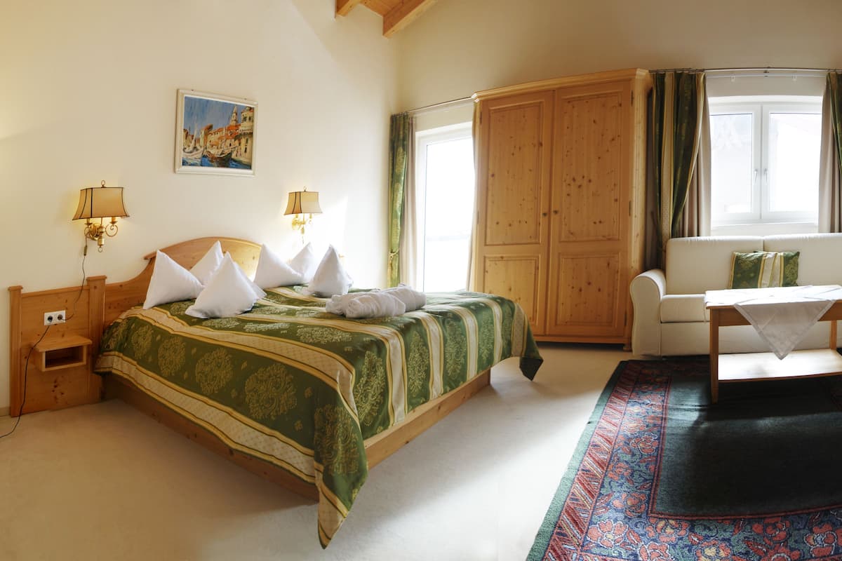 Una habitación con una cama, un sofá, un armario de madera, una mesa y un ventanal con cortinas.