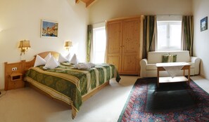 Una habitación con una cama, un sofá, un armario de madera, una mesa y un ventanal con cortinas.