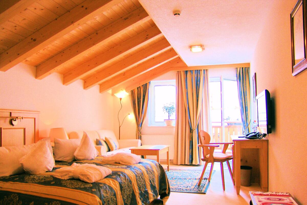 Una habitación de hotel con cama, escritorio, silla, televisor y ventana con cortinas.