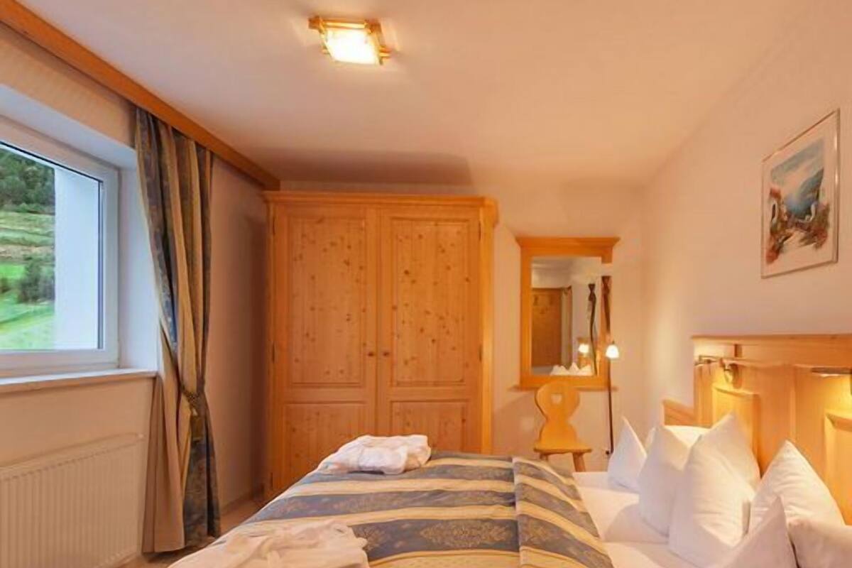 Un dormitorio con cama, armario de madera y ventana con cortinas.