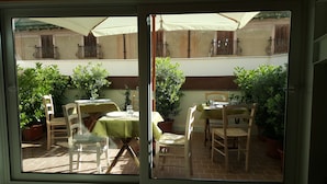 A patio area with two tables and chairs, surrounded by potted plants and a view of a building with shutters. - PalermiT'amo (Palermo)