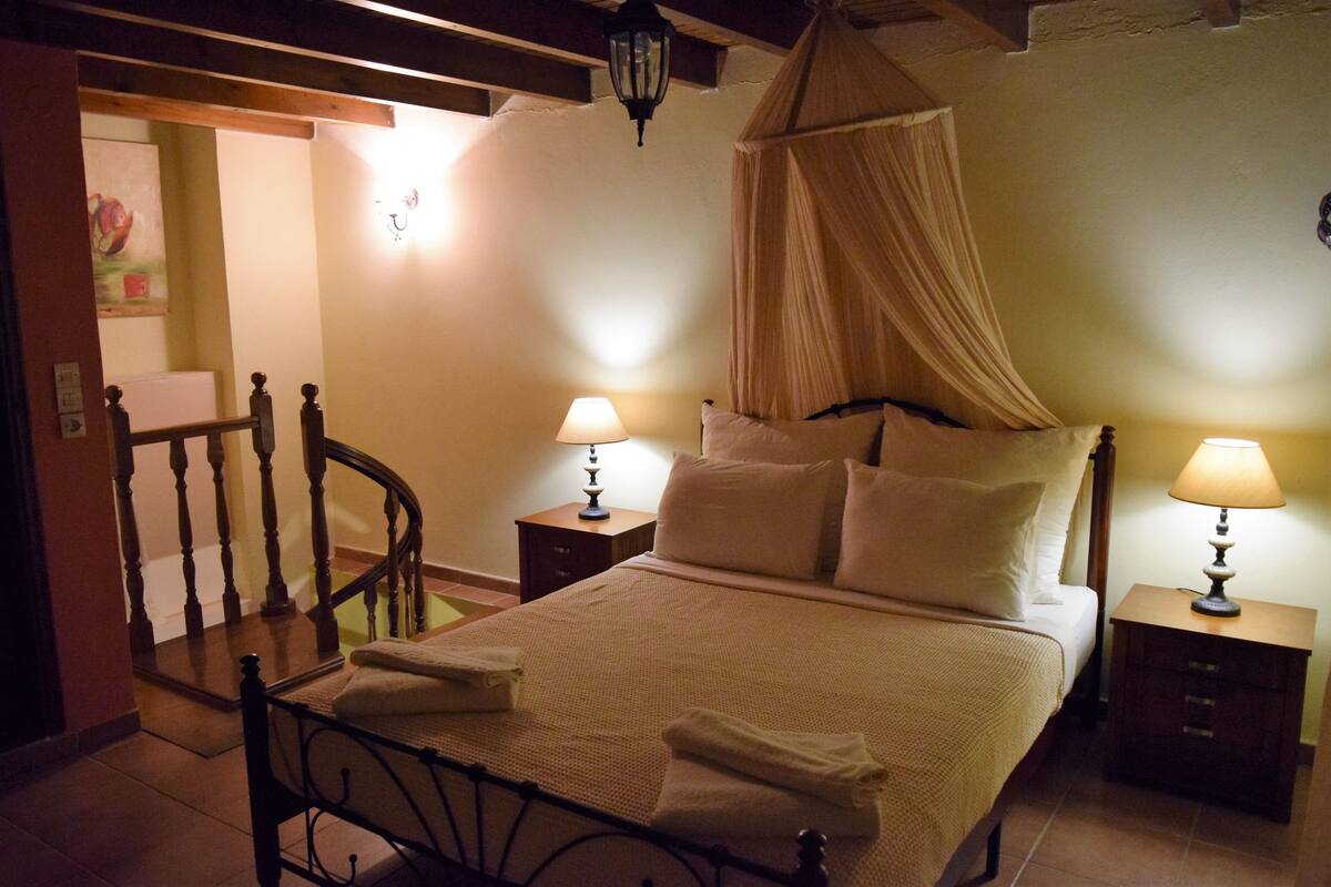 Un dormitorio con una cama con dosel, dos mesitas de noche con lámparas y una silla de madera.