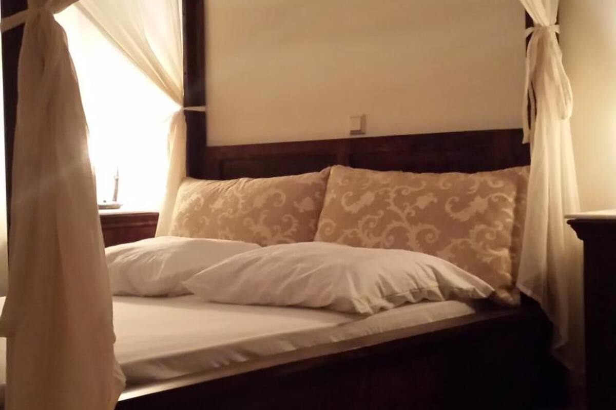 Una cama con dosel, cabecera y mesita de noche.