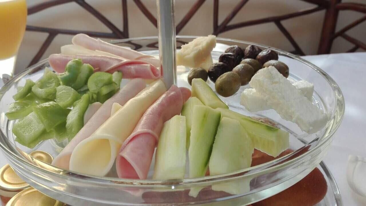 Una tabla de cristal con diversos alimentos, como verduras cortadas, queso y aceitunas.