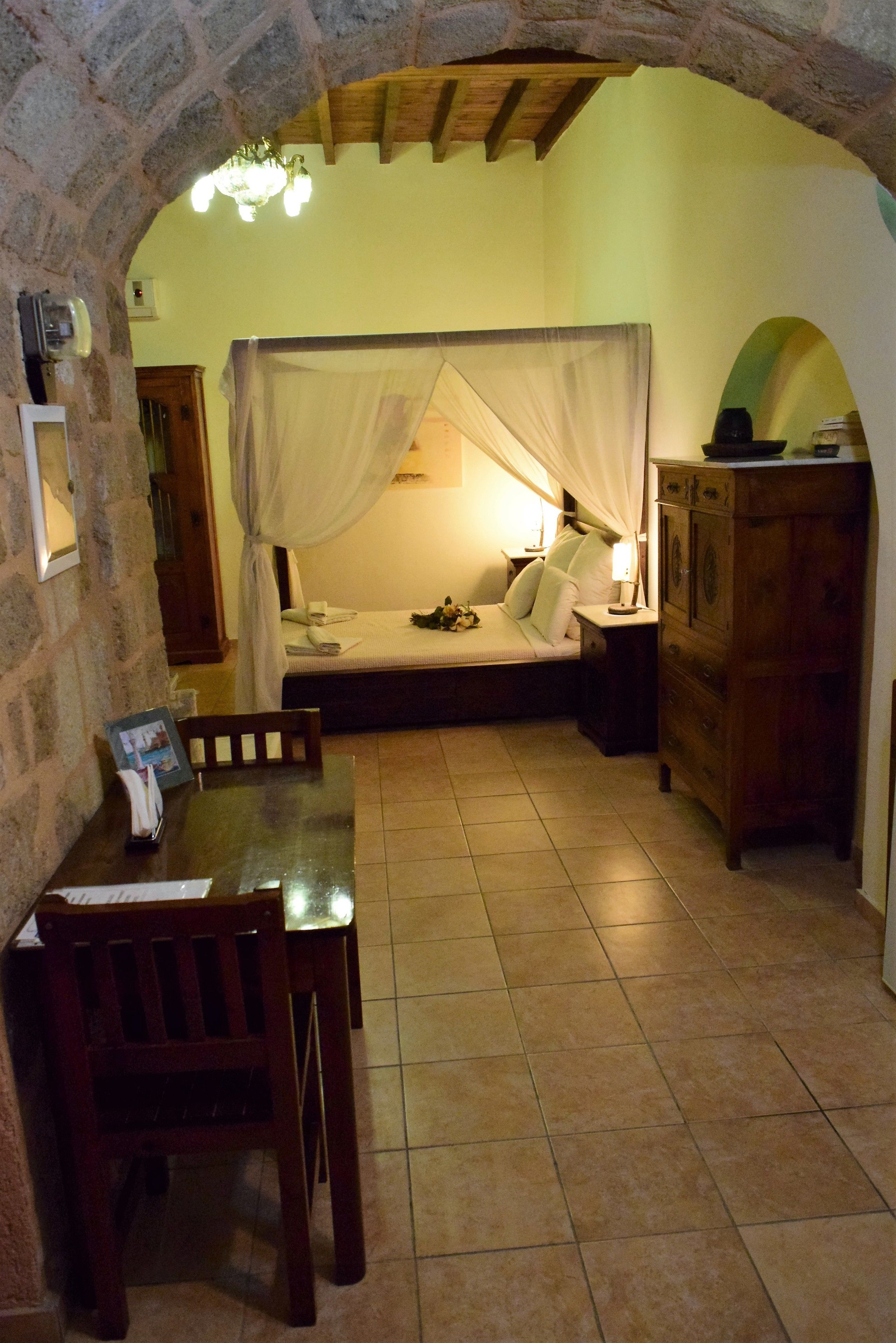 A bedroom with a bed under a canopy, a wooden dresser, a nightstand, and a table with chairs.
