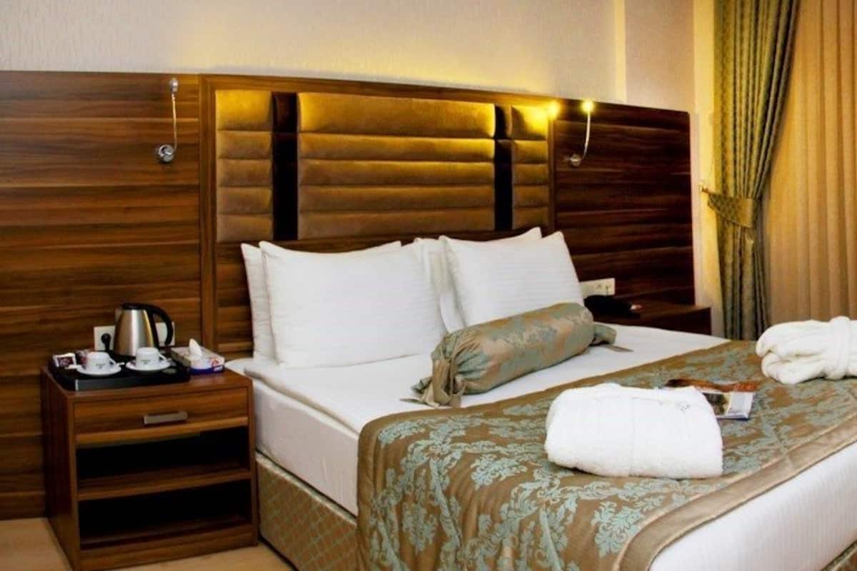 Habitación de hotel con una cama grande, un escritorio de madera, una silla, un televisor de pantalla plana y una mesita de noche con una lámpara y una taza.