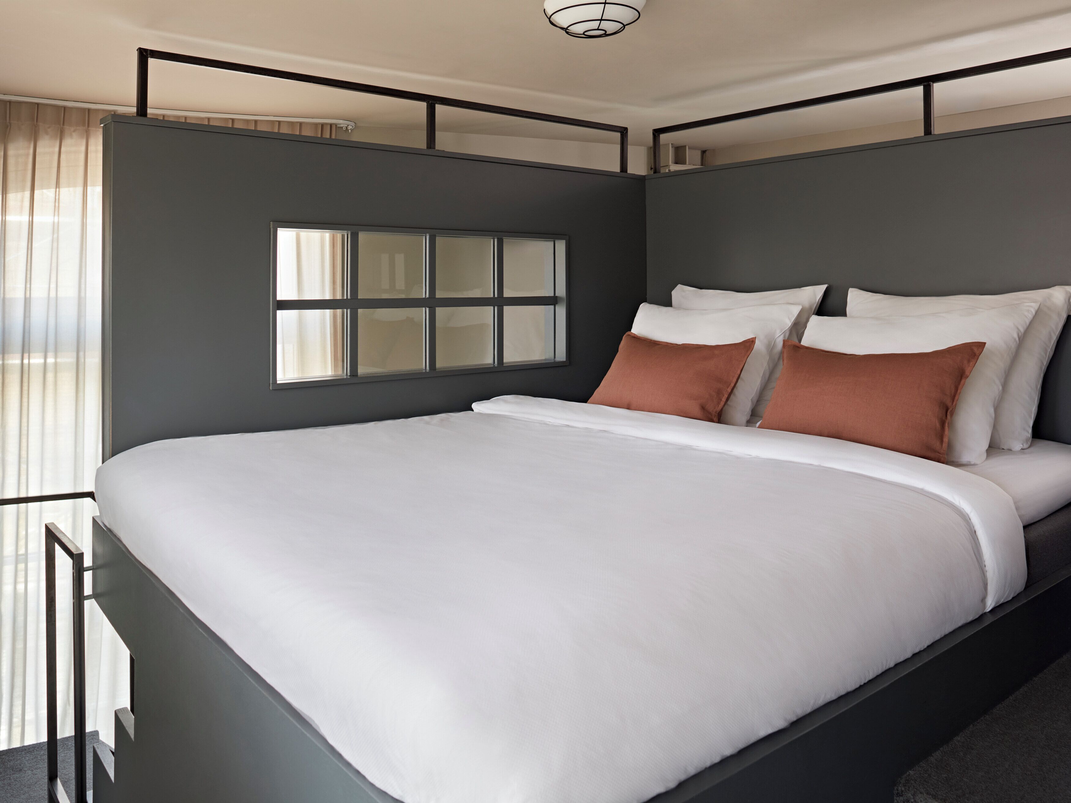 A modern bedroom with a large bed, a window with blinds, and a ceiling light.