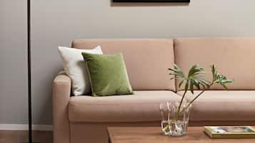 A beige sofa with two pillows, a glass vase with a plant, and a book on a wooden coffee table.