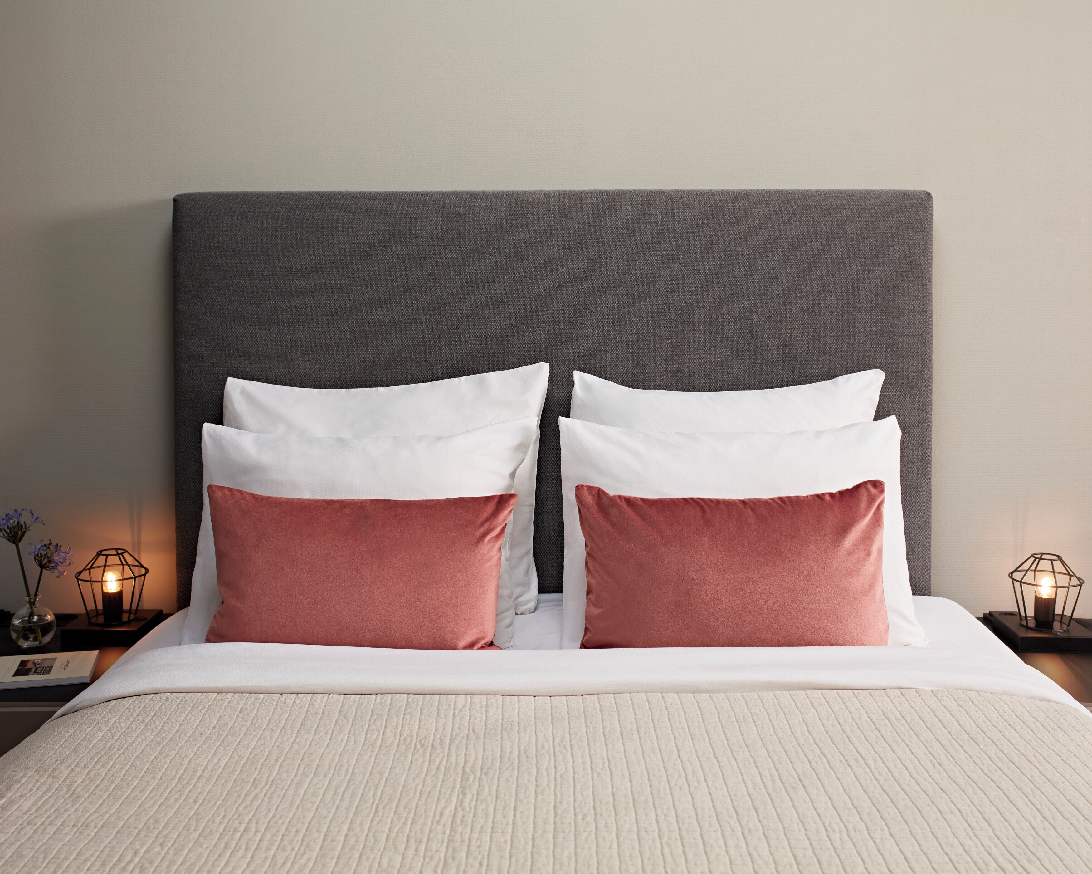 A neatly made bed with a grey headboard, two white pillows, and two pink pillows.
