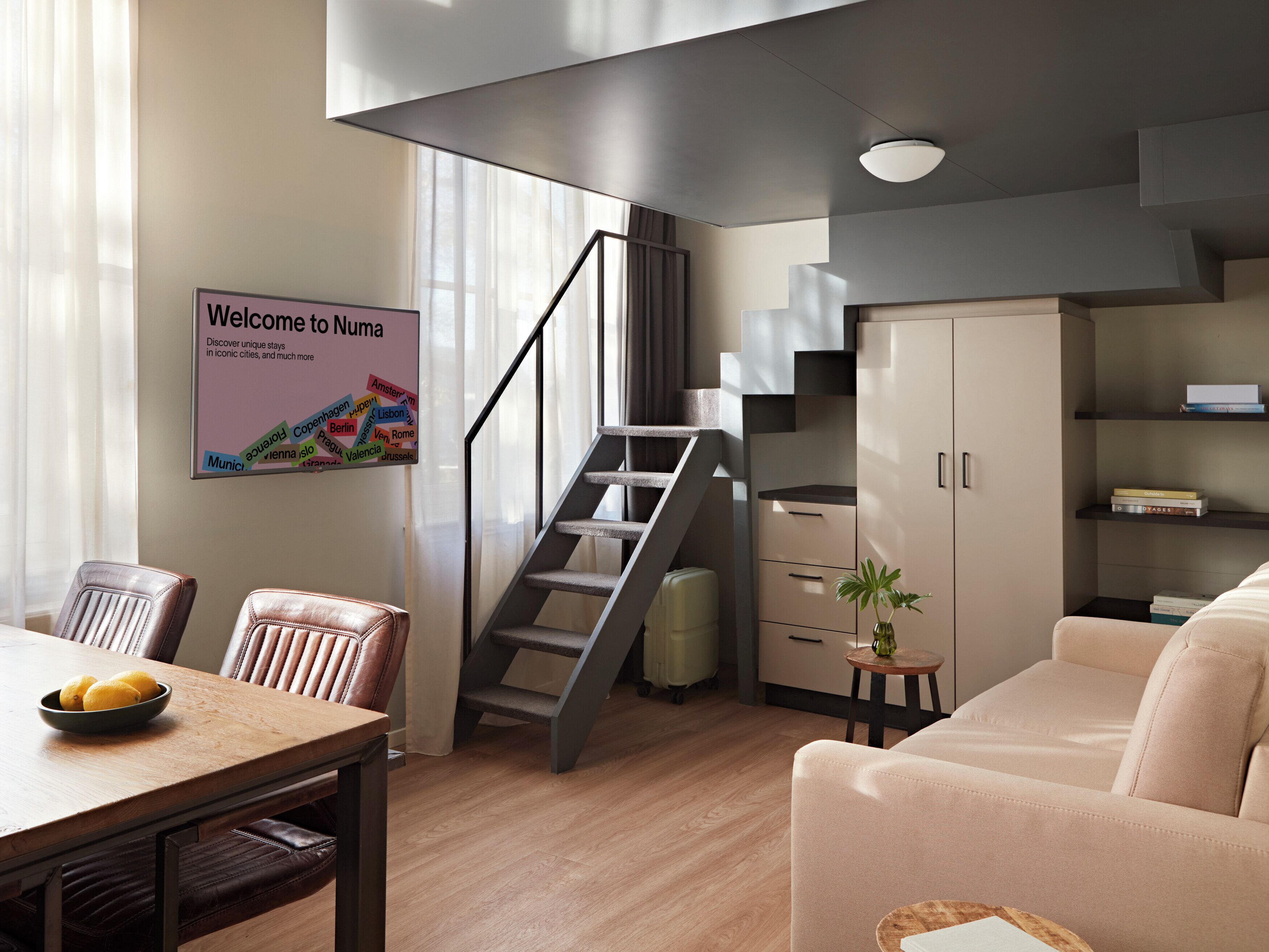 Een moderne woonkamer met een eethoek, een trap en een bord dat gasten verwelkomt bij Numa.