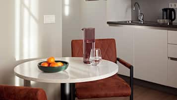 A modern kitchen with a round dining table, a bowl of oranges, a glass pitcher, and a glass of water.