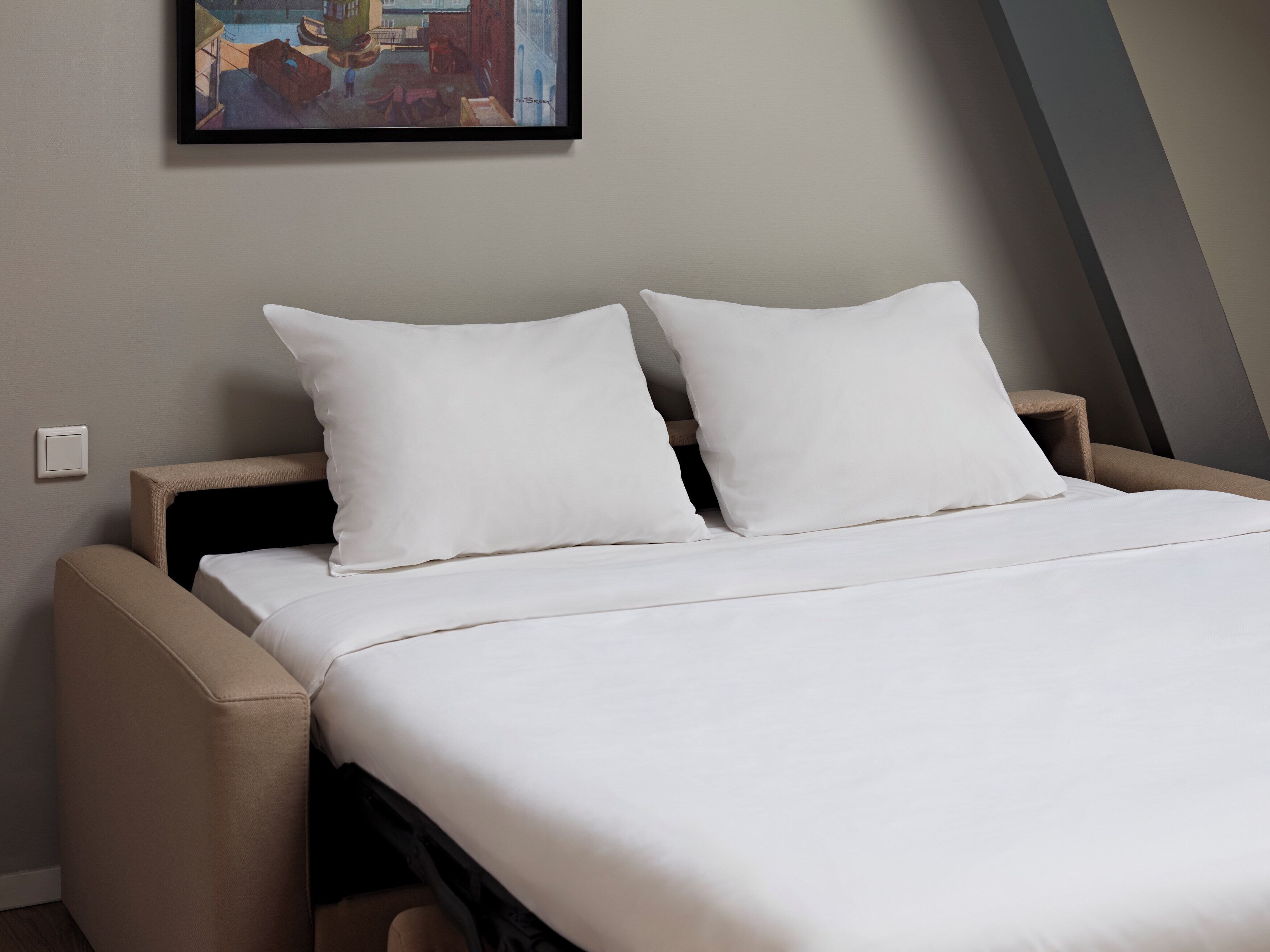 Un letto rifatto con lenzuola bianche in una stanza moderna con un quadro appeso al muro.