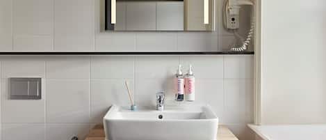 A bathroom with a white sink, wooden vanity, and a mirror above it. There are two bottles of lotion and a toothbrush holder on the vanity.