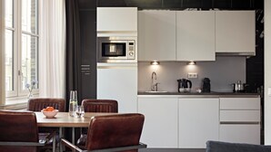 Eine moderne Küche mit weißen Schränken, einer Edelstahl-Mikrowelle und einer Kaffeemaschine. Ein Esstisch mit Stühlen und eine Vase mit Blumen sind ebenfalls vorhanden.