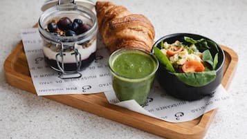 A wooden tray with a jar of yogurt parfait, a croissant, a bowl of salad, and a green smoothie.