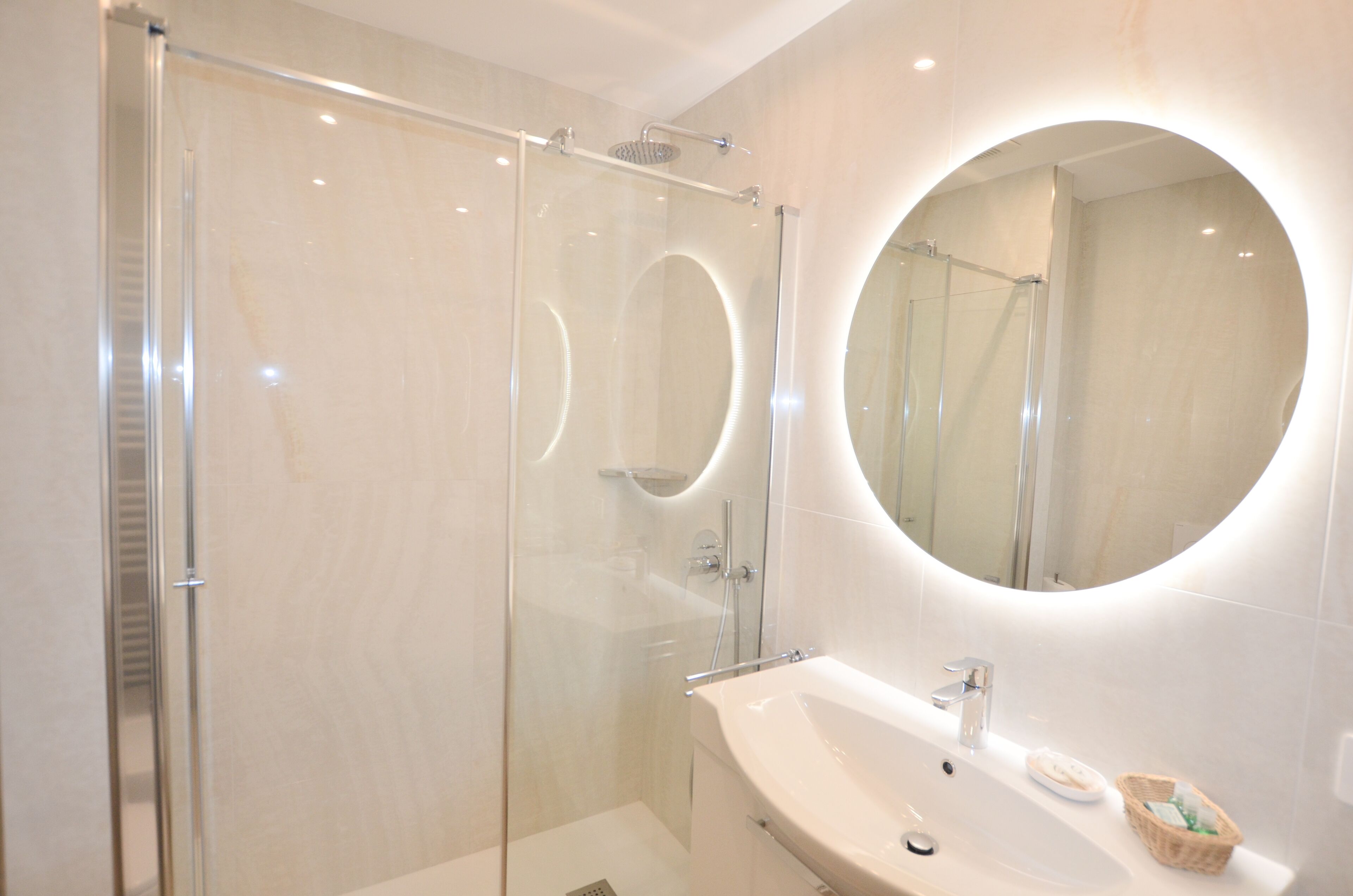 A modern bathroom with a glass-enclosed shower, a round mirror, and a white sink.