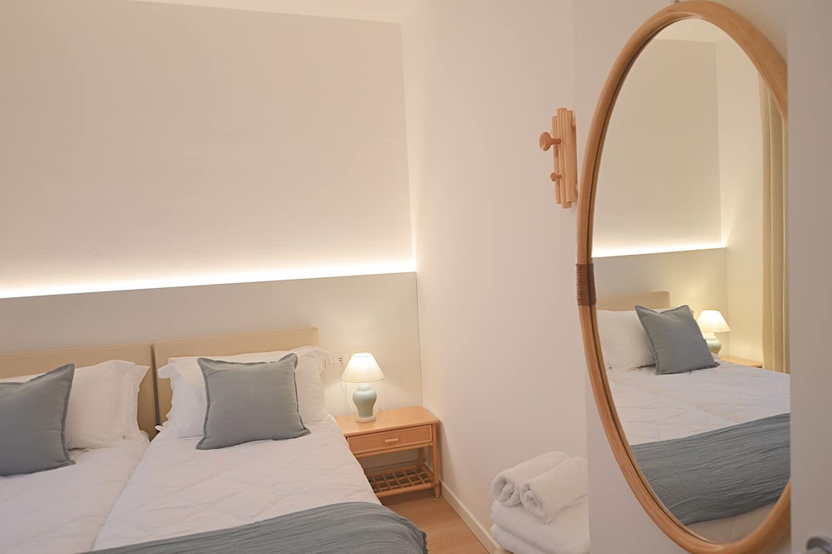 A hotel room with two beds, a nightstand with a lamp, a mirror, and a towel rack.