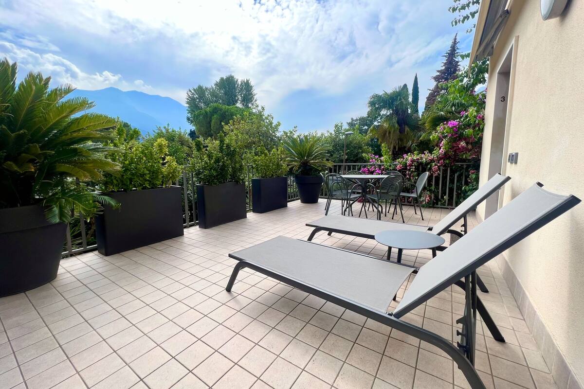 A patio with tiled flooring, lounge chairs, a table, and potted plants.