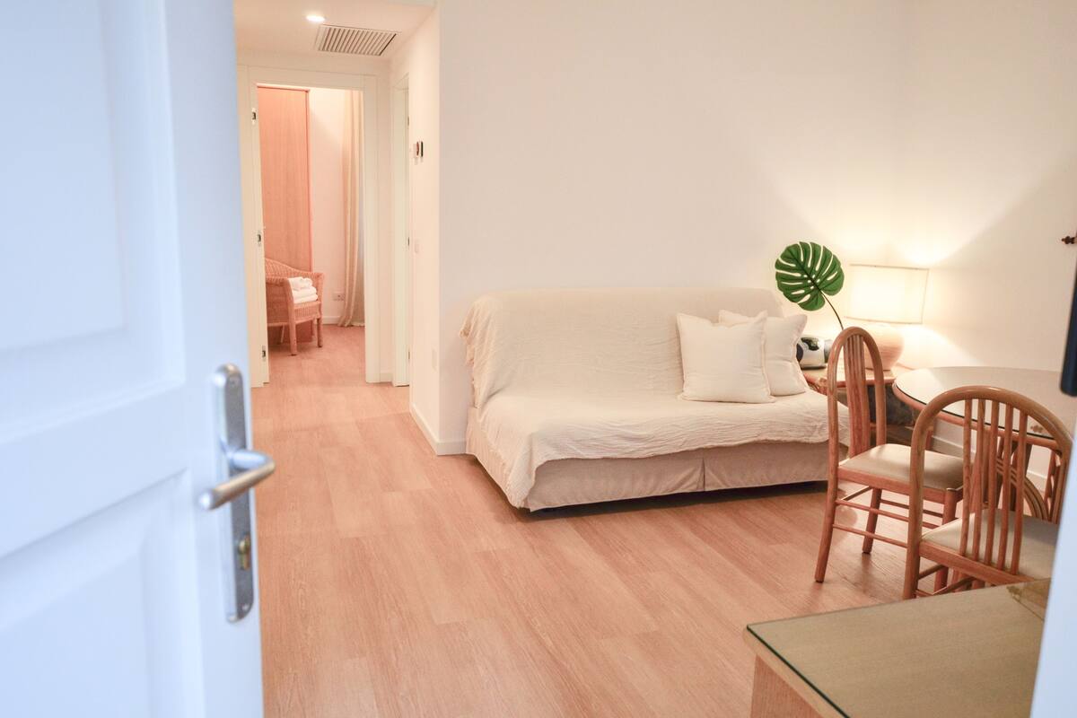 A room with a beige sofa, a wooden chair, a small table, and a lamp.