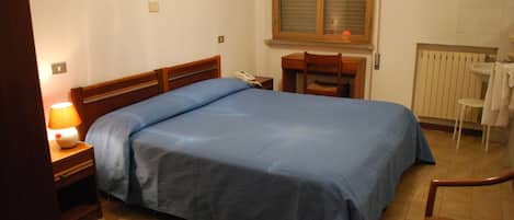 Une chambre à coucher comprenant un lit, une table de chevet, une lampe, une chaise et une fenêtre avec des stores.