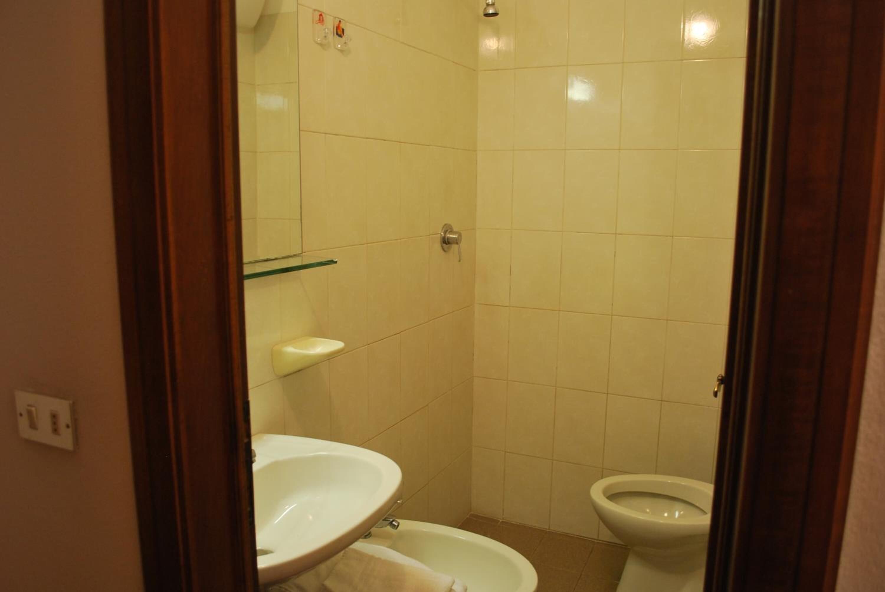 A small, tiled bathroom with a toilet, a sink, and a mirror.