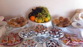 A buffet table with various food items including fruits, pastries, and packaged snacks.