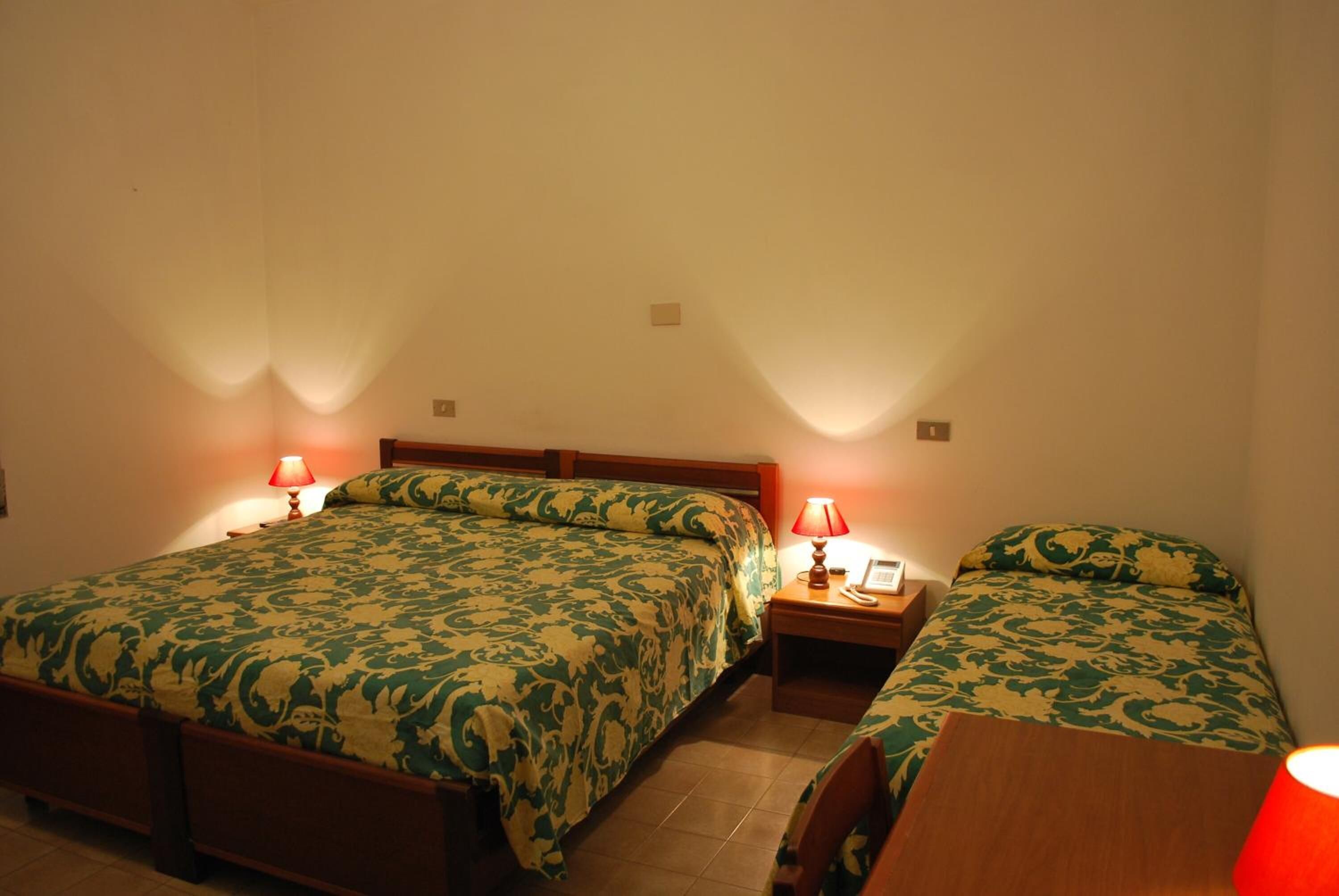 Ein Zimmer mit zwei Einzelbetten, jeweils mit Holzrahmen und Bettwäsche mit grünem Muster. Nachttische mit Lampen und ein kleiner Tisch mit einem Telefon sind vorhanden.