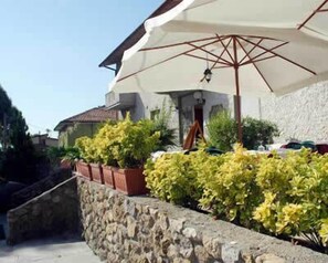 A stone wall with potted plants and a white umbrella.