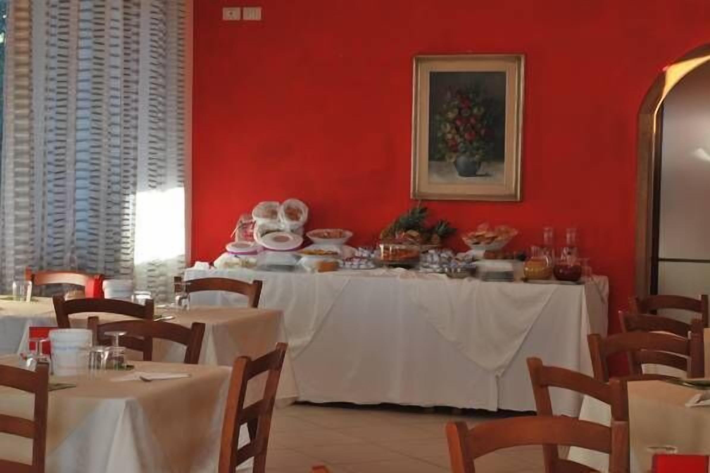 Un coin repas avec des tables dressées pour le repas, un tableau accroché au mur et une fenêtre avec des rideaux.