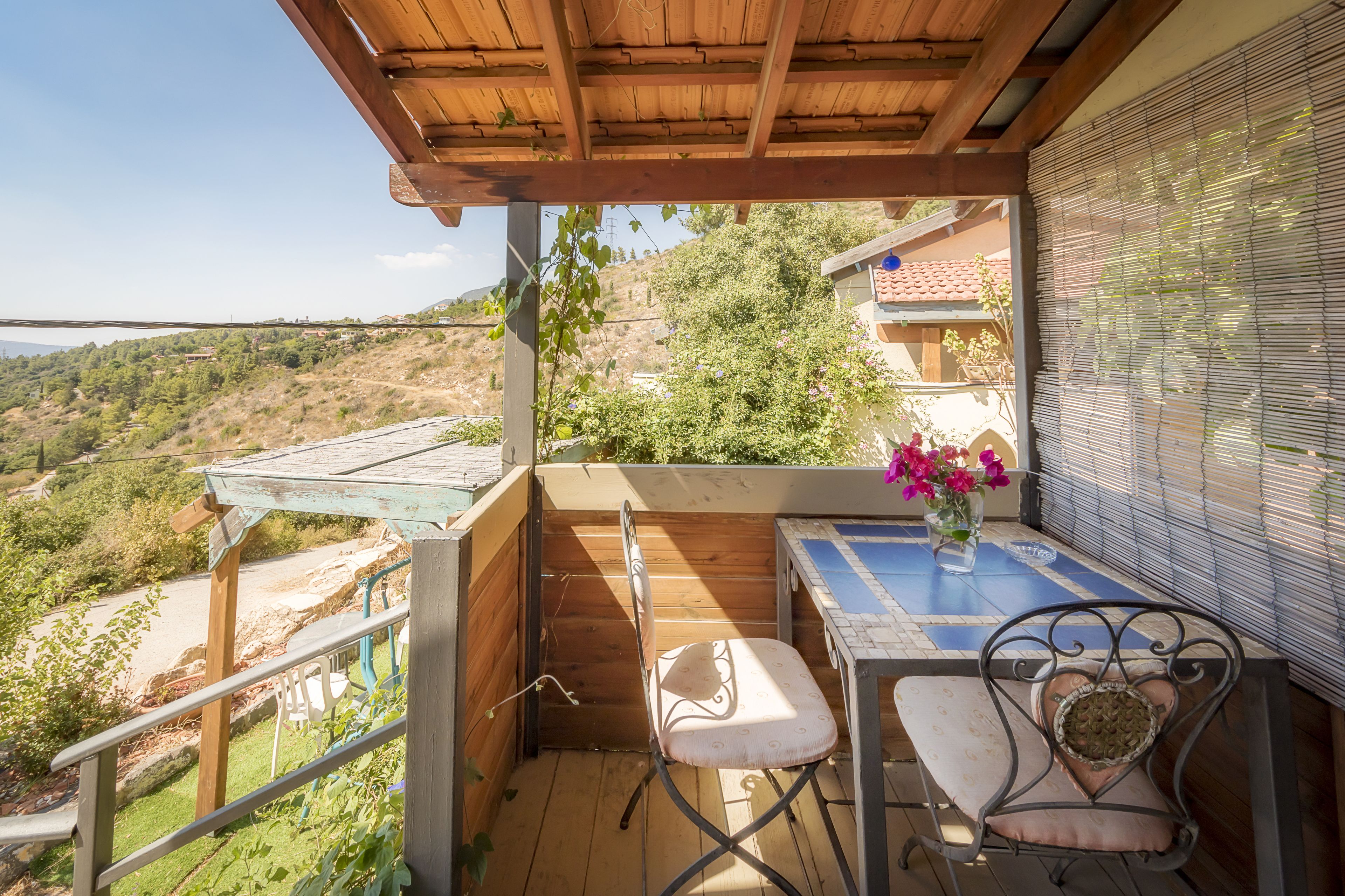 A balcony with a wooden pergola, a table with a vase of flowers, and a chair.