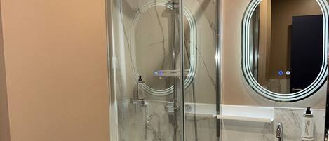 A modern bathroom with a glass-enclosed shower, a white sink with a mirror, and a patterned floor.