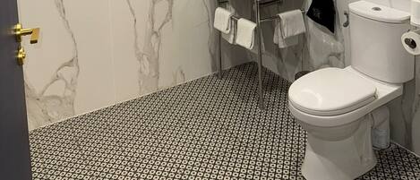 A bathroom with a marble wall, a sink, a toilet, and a towel rack.