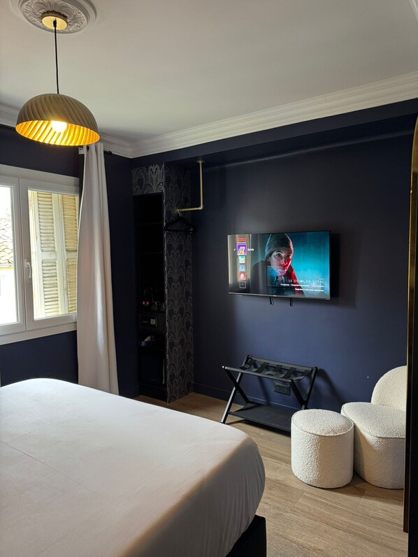 A modern hotel room with a large bed, a TV mounted on the wall, a bench, and two ottomans. - Hôtel La Caravelle (Aix-en-Provence)