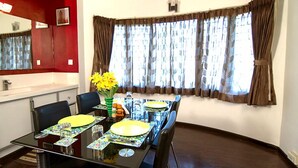 A dining area with a glass table, chairs, and a vase of yellow flowers. - Phoenix Hospitality Services (Chennai)