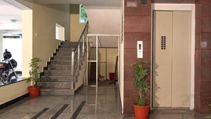 A lobby with a staircase, potted plants, and an elevator. - Phoenix Hospitality Services (Chennai)